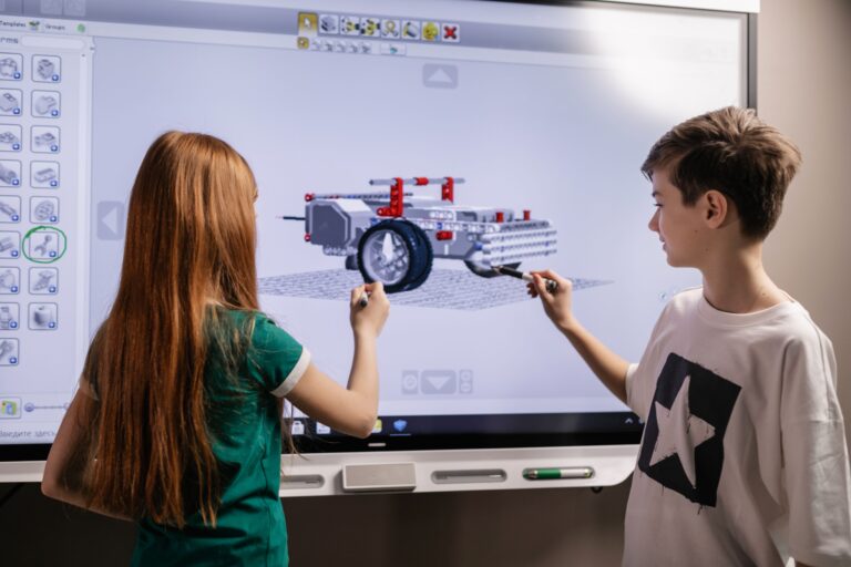 Dzieci w szkole podstawowej uczące się robotyki i programowania na tablicy interaktywnej